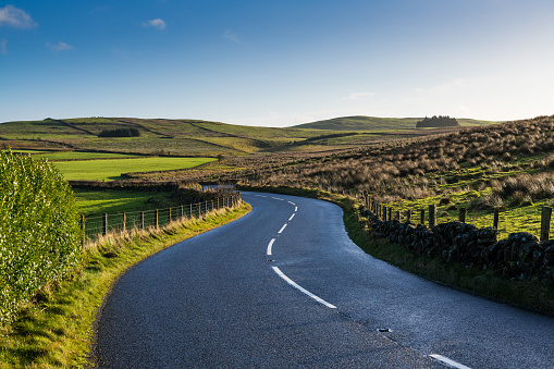 A scenic country road winding through the lush green hills and fields of Northern Ireland's serene rural landscape