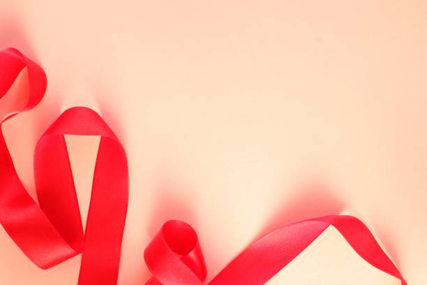 istock Curved wavy silk satin red ribbon on beige background with copy space for text. Holiday, celebration, anniversary, birthday gift decoration concept 1473730814