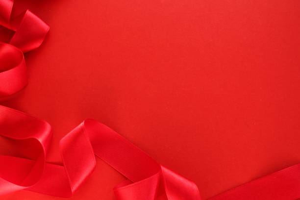 istock Curved wavy silk satin red ribbon on red background with copy space for text. Holiday, celebration, anniversary, birthday gift decoration concept 1473730870
