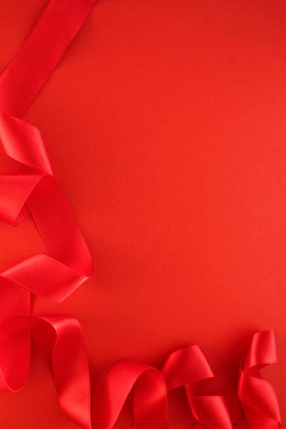istock Curved wavy silk satin red ribbon on red background with copy space for text. Holiday, celebration, anniversary, birthday gift decoration concept 1473730905