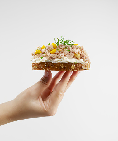 Woman holding tuna sandwich with whole wheat bread.