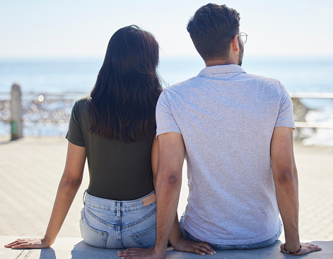 Beach, view and love with a couple on the promenade together outdoor during summer by the sea or ocean. Back, date and vacation with a man and woman bonding while on holiday by the coast or water