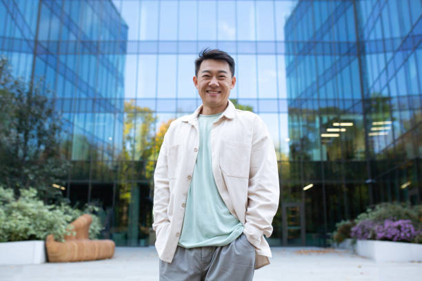 istock Portrait of a young handsome successful Asian male programmer, freelancer, student. Standing in front of office center outside, hands in pockets, smiling and looking at camera 1473735687