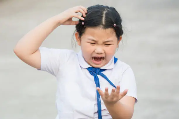 Child student fierce, mad, maniac, maniacal, rabid, wild because lice on the head,she is symptoms itching,scratch head for lice and frightened,agape