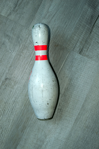 An old used bowling pin lays on its side on a grey floor.