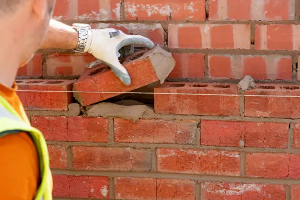 Photo of Bricklayer laying bricks on mortar on new residential house construction, Last brick to fill the gap