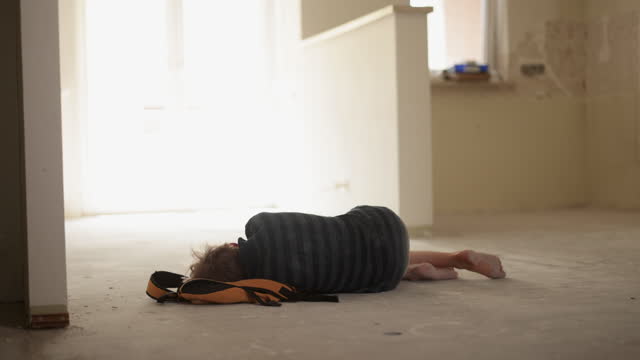 Depressed teenage boy sleeping on the floor in the empty, damaged apartment