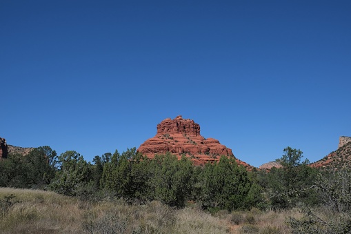 Bell rock formation which is red sandstone at different times of day and from different distances against a blue sky surrounded by scrub brush and local trees. Located in Sedona, AZ is perfect area for outdoor enthusiasts and hikers.