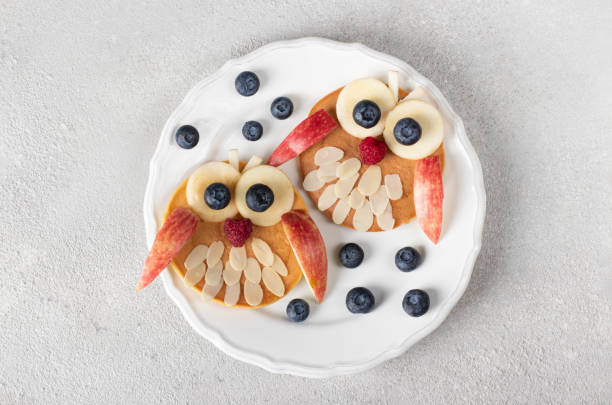 istock Fun breakfast for kids - owl shaped pancakes with blueberry, raspberry, apple and almond on white plate, Top view 1473744312