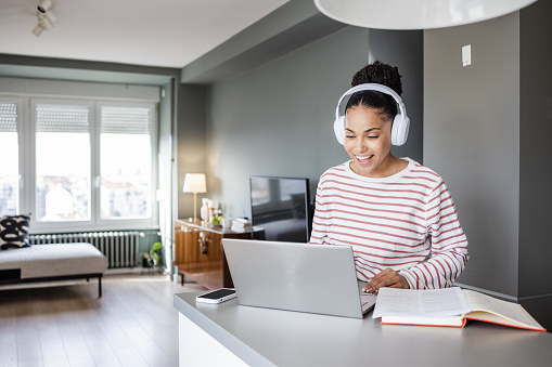 Young woman at home. She is attending an online meeting. A woman with wireless headphones is presenting ideas to her team.