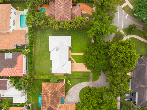 Aerial drone shot of suburb in Coral Gables city with large tropical greenery around, modern houses with elegance and style, summer weather, blue sky