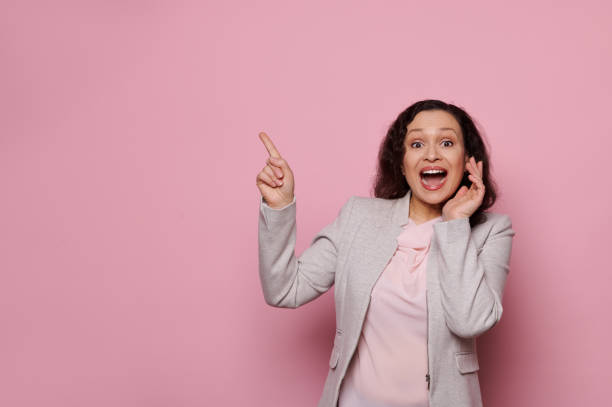 istock Amazed pretty woman pointing forefinger at copy space for your ads, looking at camera, isolated over pink background 1473751261