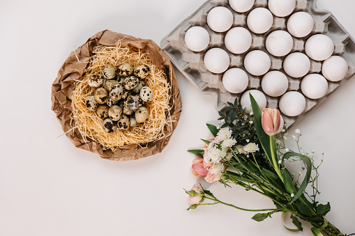 Nest with quail eggs, bouquet of flowers and white eggs in a box. Easter preparation