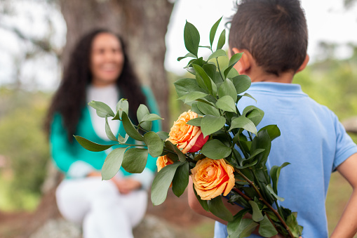 A cute little boy hides a bouquet of roses he has prepared for his mother.
