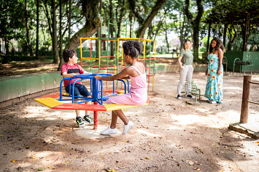 Kids playing in a merry-go-round while their mothers look in a park