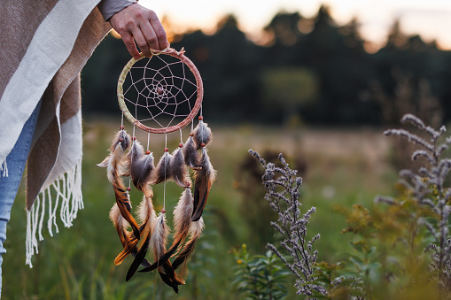 Woman with poncho holding dream catcher outdoors. Spirituality and harmony between people and nature