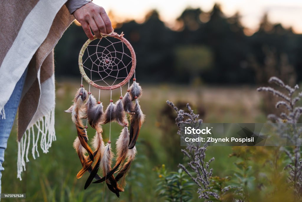 Woman with poncho holding dreamcatcher outdoors Woman with poncho holding dream catcher outdoors. Spirituality and harmony between people and nature Dreamcatcher Stock Photo