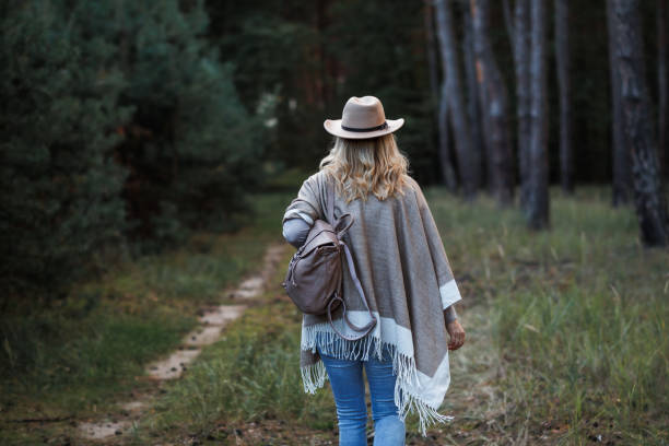 Boho woman with poncho, cowboy hat and backpack walking in forest
