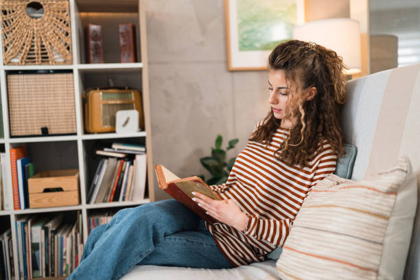 istock Young Caucasian woman reading a book at her home 1473757964