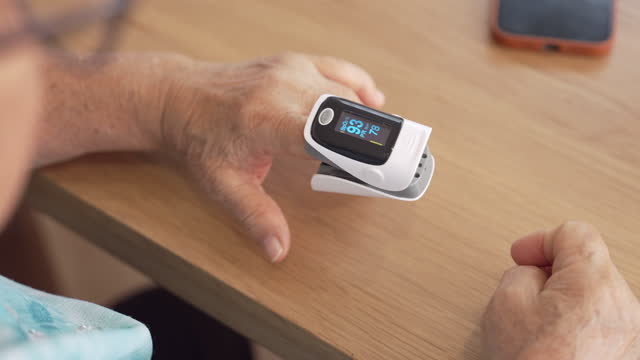 Close-up of Asian senior woman measuring oxygen level with fingertip pulse oximeter at home.