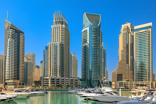 Dubai, United Arab Emirates - In view are boats and motor yachts moored on Dubai Marina in the morning sunlight. In the background are modern skyscrapers that house offices, apartments and hotels. Photo shows off a modern luxurious lifestyle that is synonymous with the Persian Gulf city of Dubai. Horizontal format. Note to Inspector: All boat registration numbers have been removed.