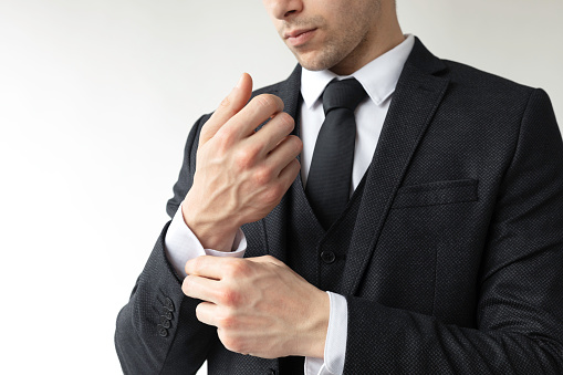Midsection of unrecognizable businessman is getting ready for business meeting. He is buttoning cuffs in front of white background.