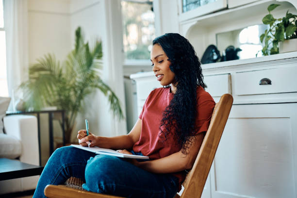 istock Young African American woman writing a diary while relaxing at home. 1473763170