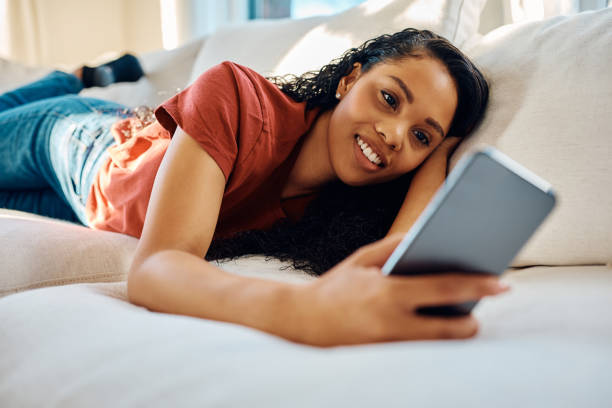 istock Happy black woman using mobile phone while relaxing on the sofa. 1473763251