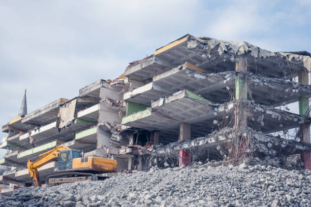 A crane working on a building demolition. The crane stands on the rubble and the destroyed building is visible in the blurred background.