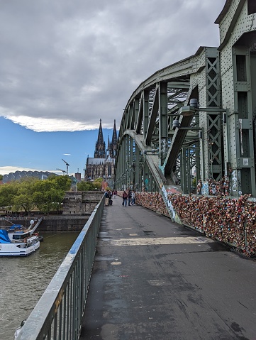 Looking across the Hohenzollern bridge in Cologne onto the Cologne Cathedral in the center distance, Museum Ludwig and Rhine river to the left. To the right a wall of love locks mounted to the fence along the bridge is visible and extending to the far distant end of the bridge.