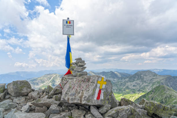 Top of Mt. Peleaga with Romanian flag and stack of stones. Granite rocks with trail marking.