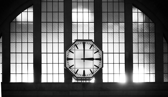 Closeup of a clock hanging of a window of a traditional train station in Europe, the afternoon sunlight passes through the window glass making reflection. The clock marks the hour three o'clock