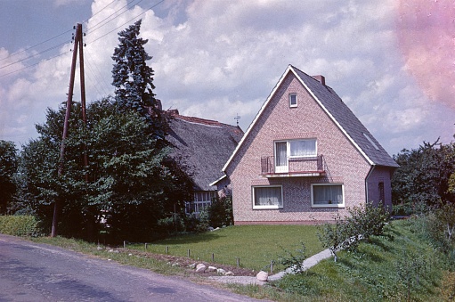 Schleswig Holstein, Germany, 1973. Home ownership. Detached house with clinker facade and meadow next to an old barn.