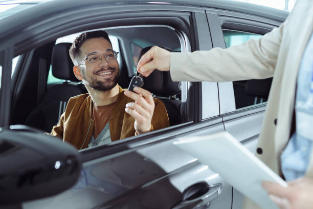 un jeune homme achète une nouvelle voiture - car car rental car dealership key photos et images de collection