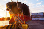 A cargo ship moored to the mooring bollard of the seaport with ropes.