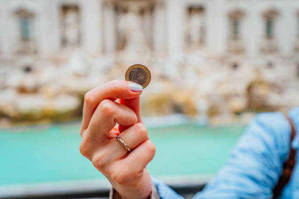 une femme tenant une pièce de monnaie devant la fontaine de trevi - euro symbol caucasian europe european culture photos et images de collection