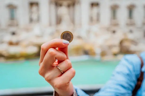 Close-up of a woman tourist hand holding a coin in front of the Trevi Fountain and making a wish in Rome, Italy