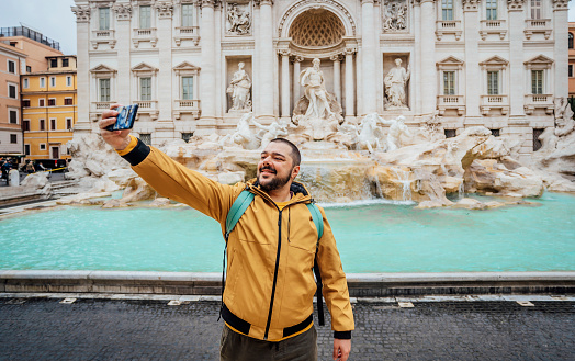 Young man taking a selfie in front of the di Trevi Fountain in Rome