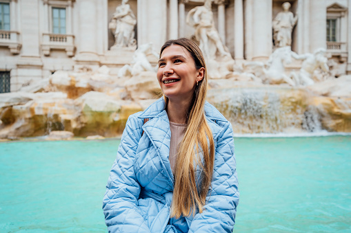 Young happy woman tourist in front of the famous iconic Trevi Fountain in Rome, Italy