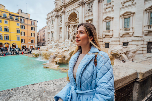 Young happy female tourist visiting the famous iconic Trevi Fountain in Rome, Italy