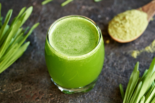 A glass of green barley grass juice with fresh blades and powder