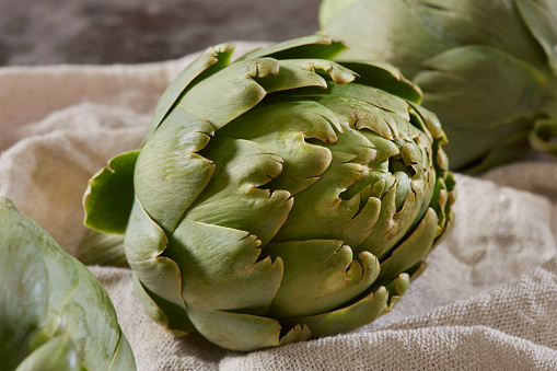 Pile of green Spanish or Italian Artichokes on the metal rustic plate and gray concrete background, close up