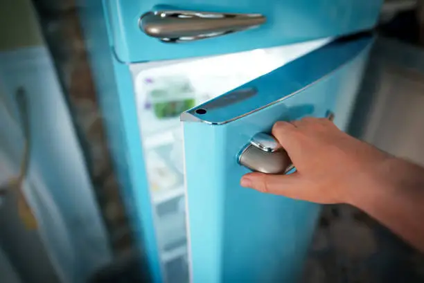 Photo of Man opening door of retro refrigerator freezer.