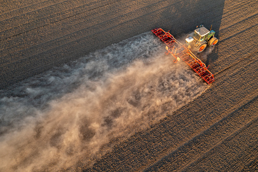 Agricultural tractor with a red planter plants grain corn in spring, creates a large dust trail due to drought.