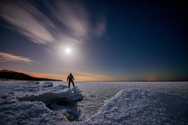 istock Traveler on the seashore covered with ice under a starry sky with clouds and moon 1473794227