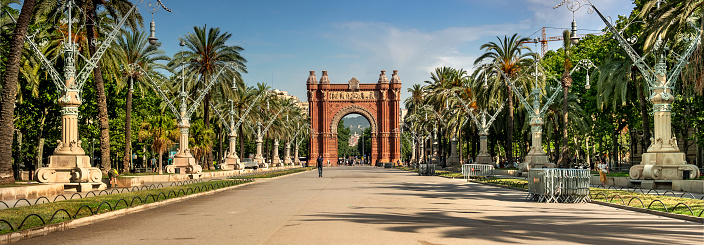 Barcelona, Spain - June 13, 2022:  People walk by the Arch of Triumph in the district of downtown Promenade Passeig de Lluís Companys.  In 1888 Barcelona hosted the Universal Exhibition. The Arc de Triomf was built as the gateway to the fair which was held in the Parc de la Ciutadella.