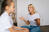 Close-up side view of angry emotional young mother scolding, raising voice, scream and gesturing with hands at stubborn difficult little child daughter at home.