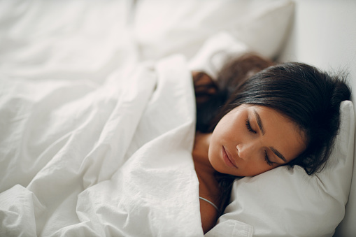 Beautiful brunette young woman covering white blanket sleep in bed at bedroom.