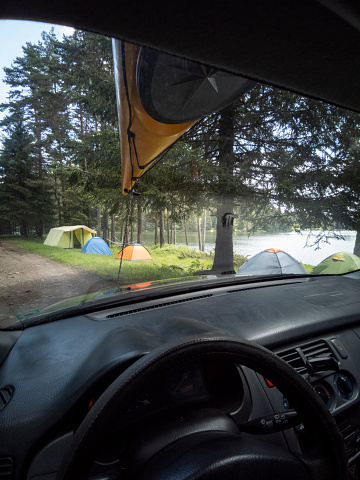 Local road trip. Driving with yellow kayak on top of the car past tent camping site, driver's point of view.