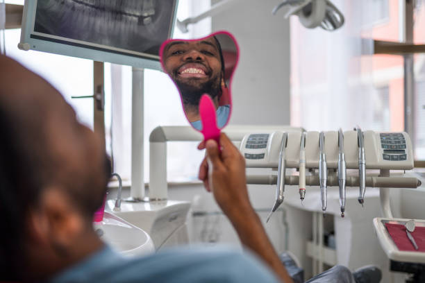 istock African-American Man Looking At Mirror With Smile In Dentist’s Office 1473800910